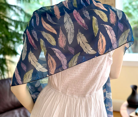 Mannequin wearing a white dress with a blue feather-patterned shawl in a room setting.