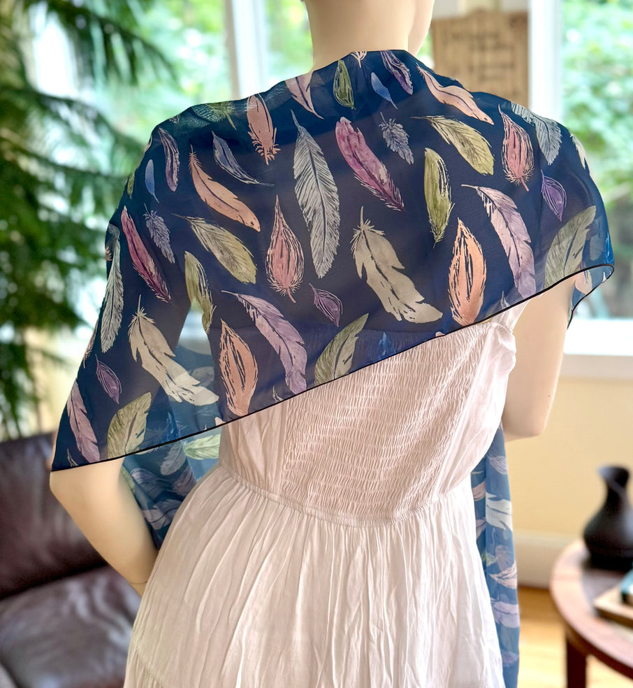 Mannequin wearing a white dress with a blue feather-patterned shawl in a room setting.